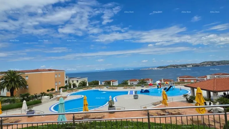 Großer Außenpoolbereich mit Meerblick, umgeben von Liegestühlen und Sonnenschirmen in einer Wohnanlage.