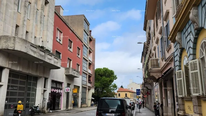 Belebte Stadtstraße mit verschiedenen Gebäuden, geparktem Auto und Fußgängern unter bewölktem Himmel.
