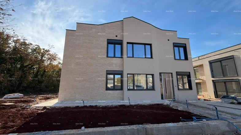 Modernes Haus im Bau mit beiger Fassade, dunklen Fenstern und vorbereitetem Gartenbereich.