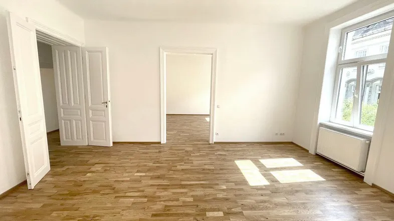Helles, leeres Zimmer mit Parkettboden und hohen Fenstern, bereit zur individuellen Gestaltung.
