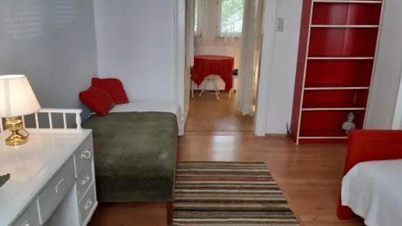 Schlafzimmer mit rotem Bücherregal und Blick durch eine Tür in einen angrenzenden Raum.