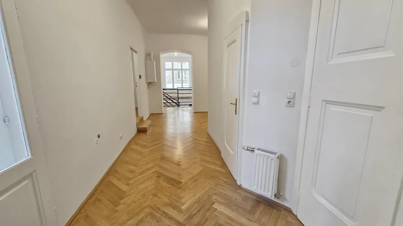 Langer, heller Flur mit Fischgrätparkett, der zu einem Treppenhaus und weiteren Räumen führt.