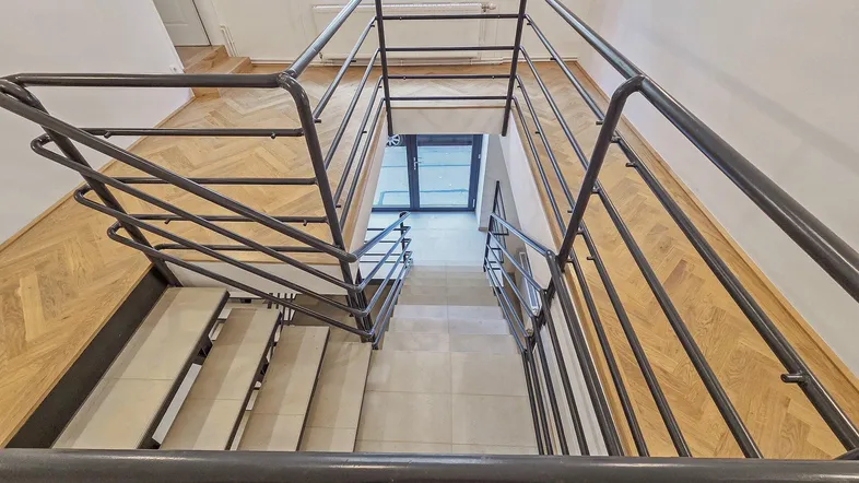 Helles Treppenhaus mit elegantem Fischgrätparkett und modernem Metallgeländer, das zu den oberen Etagen führt.