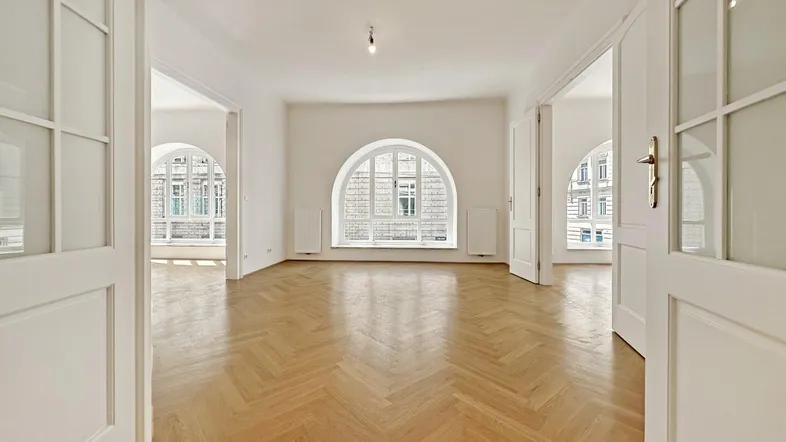 Geräumiges Zimmer mit Fischgrätparkett und hohen Rundbogenfenstern, das viel natürliches Licht hereinlässt.