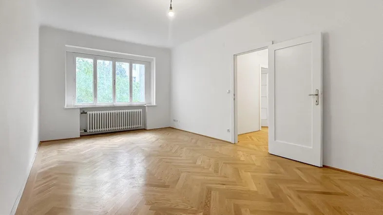 Helles Zimmer mit Fischgrätparkett und großem Fenster, ideal als Wohn- oder Schlafzimmer.