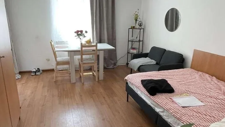 Heller Wohn- und Schlafbereich mit Holzboden, Esstisch und gemütlichem Bett.