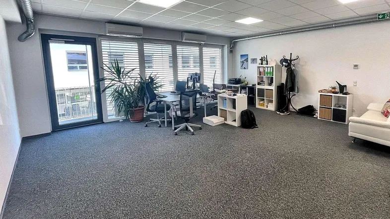 Großes, offenes Büro mit Teppichboden, mehreren Arbeitsplätzen und Zugang zu einem Balkon.