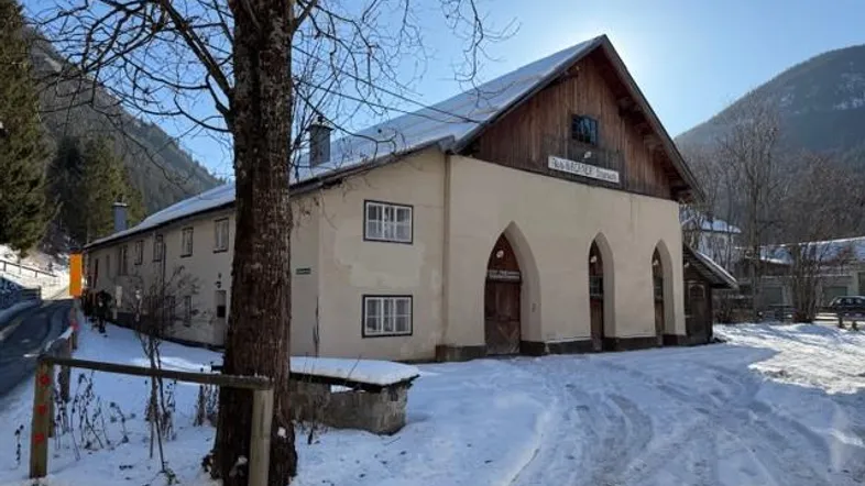 Historisches Gebäude mit markanten Rundbögen und Holzelementen, umgeben von Schnee und Bergen.