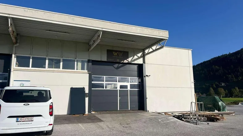 Außenansicht eines modernen Gewerbegebäudes mit Rolltor, Rampe und Parkplatz unter blauem Himmel.
