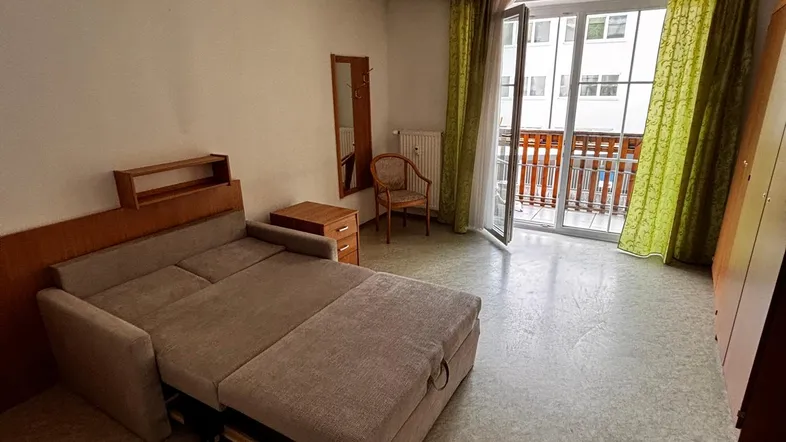 Helles Wohnzimmer mit ausziehbarem Schlafsofa und Zugang zum Balkon, mit Vinylboden.