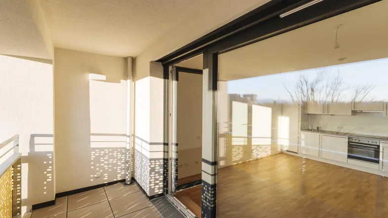 Heller offener Wohnbereich mit Parkettboden, Zugang zum Balkon und integrierter Küche.