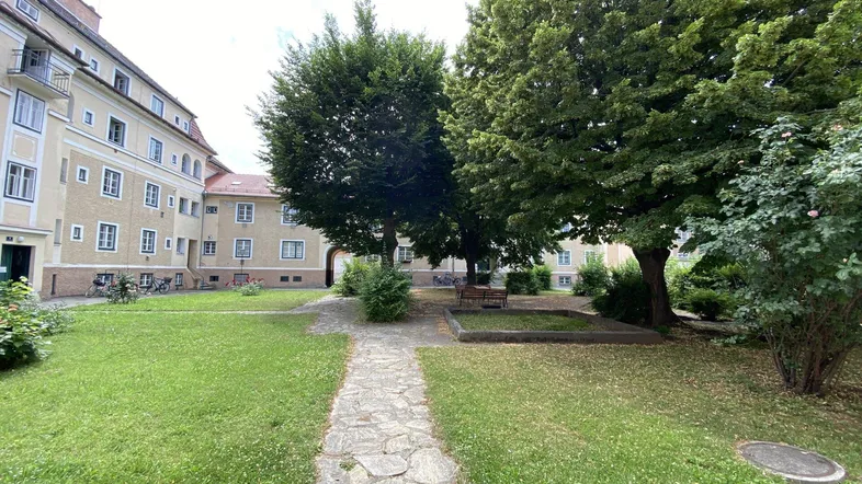 Grüner Innenhof mit Rasenflächen, Bäumen und einem Steinweg, umgeben von Wohngebäuden.