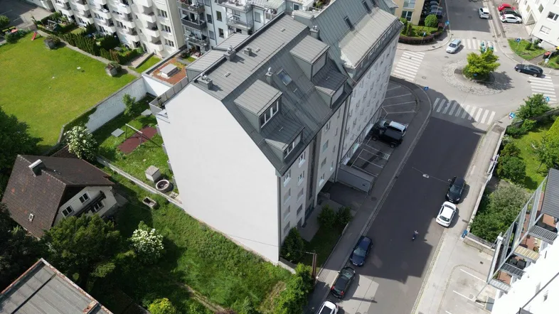 Luftaufnahme eines Wohngebäudes mit umliegender Bebauung und Grünflächen in städtischer Umgebung.