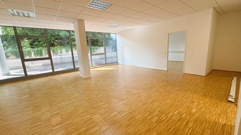 Geräumiger, leerer Büroraum mit großen Fenstern, Parkettboden und abgehängter Decke, bietet viel Tageslicht.