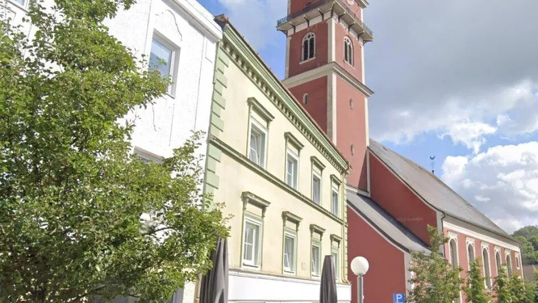 Belebte Straße mit historischen Gebäuden, einem markanten Kirchturm und Außengastronomie.