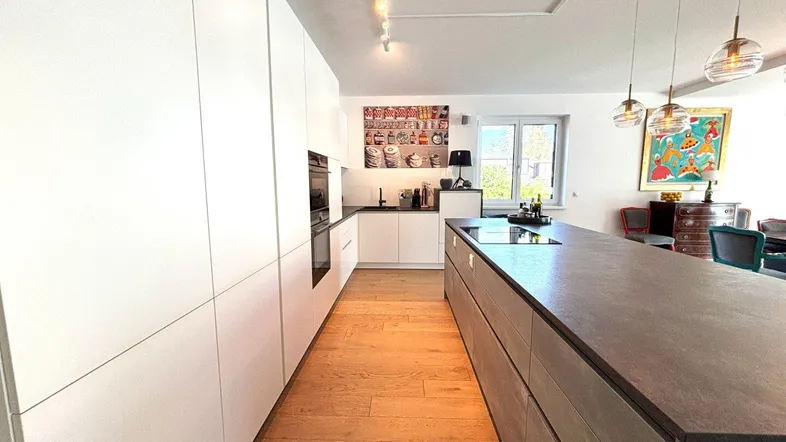 Moderne Küche mit weißen Schränken, großer Kücheninsel und Holzboden, offen zum Essbereich.