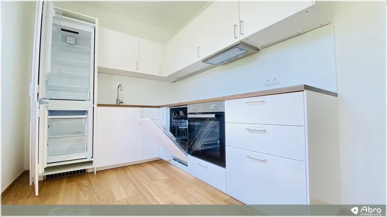 Moderne Einbauküche mit weißen Schränken, Holztheke und integrierten Geräten, inklusive offenem Kühlschrank und Geschirrspüler.