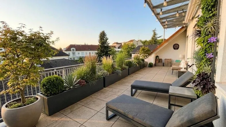 Geräumige Dachterrasse mit bequemen Liegestühlen, üppiger Bepflanzung und Blick über die Dächer.
