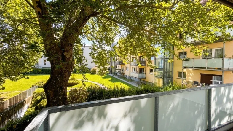 Heller Balkon mit Blick auf den grünen Innenhof und alte Bäume, ideal zum Entspannen im Freien.