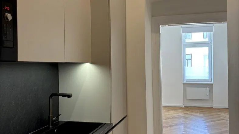 Moderne Küchenzeile mit dunkler Arbeitsplatte und integrierten Geräten, Blick in den Wohnbereich.