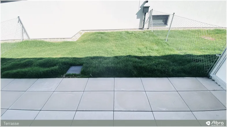 Helle Terrasse mit Fliesenboden und angrenzender Rasenfläche, ideal für Entspannung im Freien.