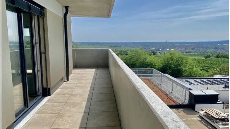 Geräumiger Balkon mit Fliesenboden und weitem Blick über die Landschaft unter blauem Himmel.