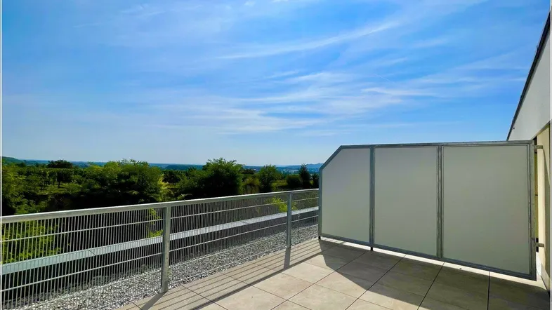 Geräumige Terrasse mit Fliesenboden und weitem Blick über die grüne Landschaft unter blauem Himmel.