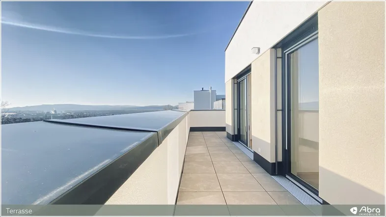 Geräumige Terrasse mit Fliesenboden und weitem Blick über die Landschaft und Berge unter blauem Himmel.