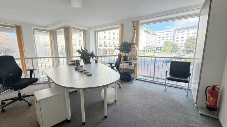 Obere Büroetage mit Teppichboden, ovalem Tisch und Blick auf die Stadt durch die Fenster.