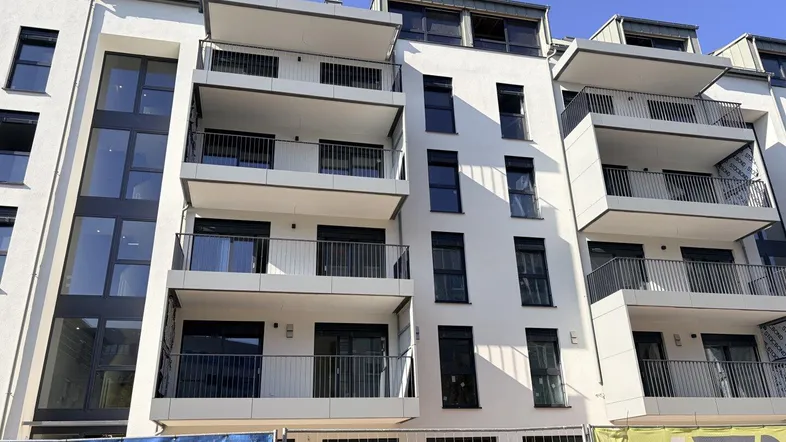 Moderne Wohnhausfassade mit Balkonen und großen Fenstern, teilweise noch im Bau.