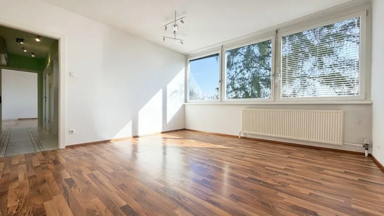 Helles, leeres Zimmer mit großen Fenstern, Holzboden und viel Tageslicht, bereit zur Einrichtung.