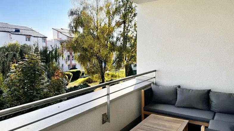Gemütlicher Balkon mit bequemen Outdoor-Möbeln und Blick ins Grüne an einem sonnigen Tag.