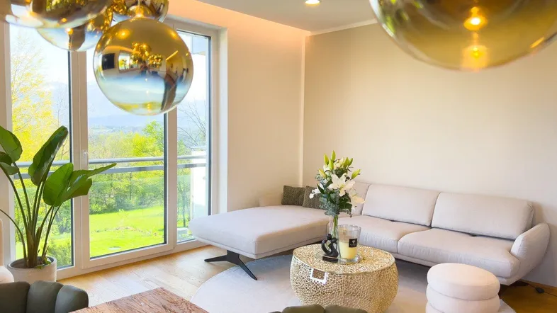 Gemütlicher Wohnbereich mit beigem Sofa, Holzboden und großen Fenstern mit Aussicht.