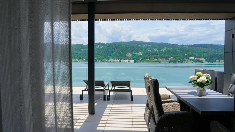 Überdachter Terrassenbereich mit Esstisch und Blick auf den glitzernden See und die bewaldeten Hügel.