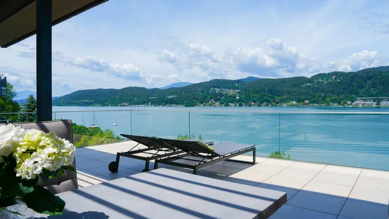 Geräumige Terrasse mit bequemen Sonnenliegen und Esstisch, bietet einen weiten Blick auf den See und die Landschaft.
