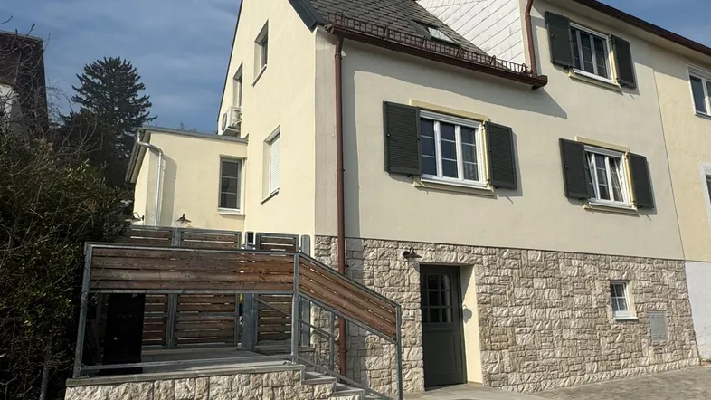 Fassade eines Hauses mit Steinsockel, Fensterläden und Außentreppe zum Eingangsbereich.