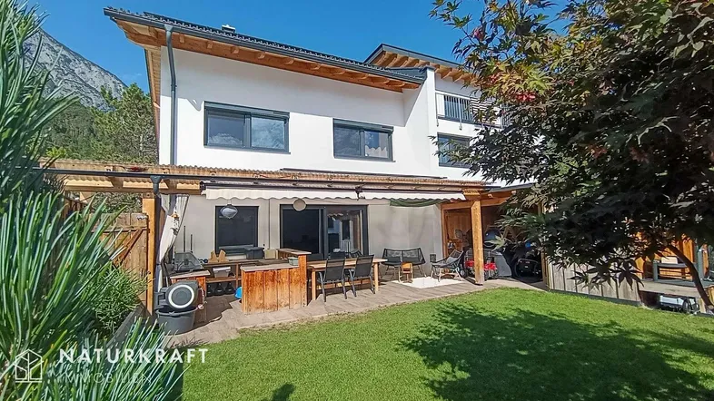 Modernes Haus mit großem Garten, überdachter Terrasse und Bergblick, ideal für Outdoor-Living.