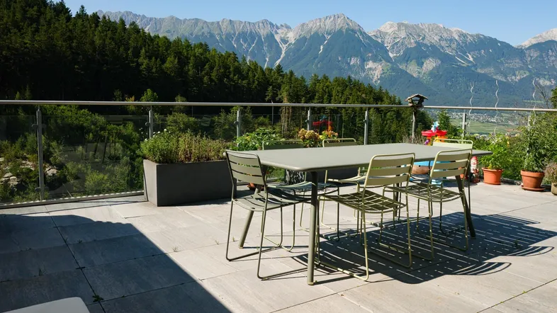Große Terrasse mit Esstisch und Stühlen, umgeben von grünen Bäumen und einem beeindruckenden Bergblick.
