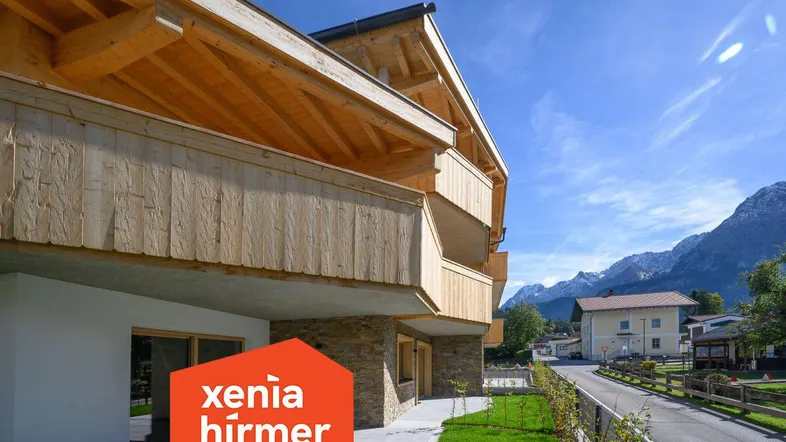 Modernes Gebäude mit Holz- und Steinfassade, umgeben von Grünflächen und Bergblick.