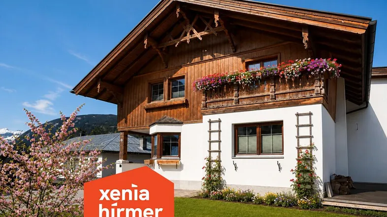 Traditionelles Holzhaus mit weißer Fassade, blühenden Blumenkästen und Bergblick in sonniger Lage.