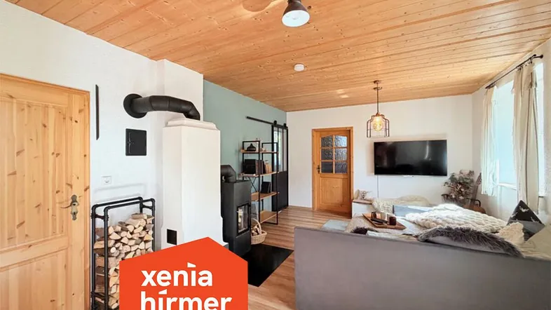 Gemütliches Wohnzimmer mit Holzbalkendecke, Kaminofen und bequemer Couch, ideal für entspannte Abende.