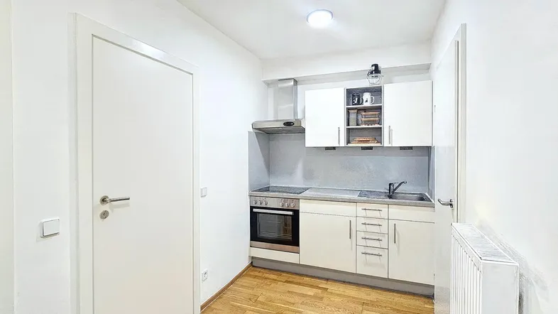 Kleine, funktionale Küchenzeile mit weißen Schränken, integriertem Backofen und Holzboden.