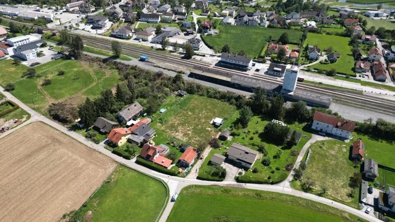 Luftaufnahme einer ländlichen Siedlung mit Häusern, Feldern, Bahngleisen und einem Bahnhof.