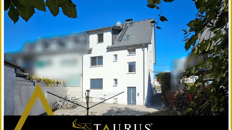 Weißes Mehrfamilienhaus mit modernem Design und Satteldach, umgeben von Grünflächen.