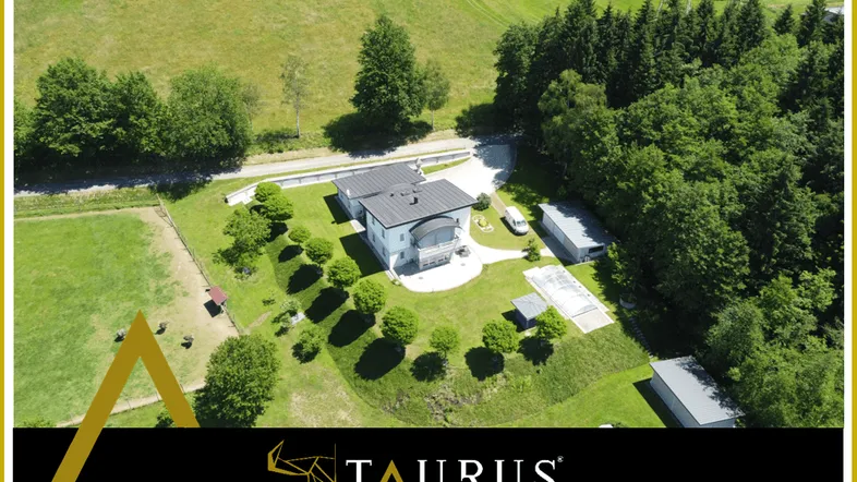 Luftaufnahme eines modernen Hauses umgeben von weitläufigen Grünflächen und Wald.