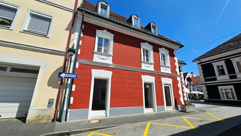 Rotes Gebäude mit weißer Fassadenverzierung und Dachgauben an einer sonnigen Straße.