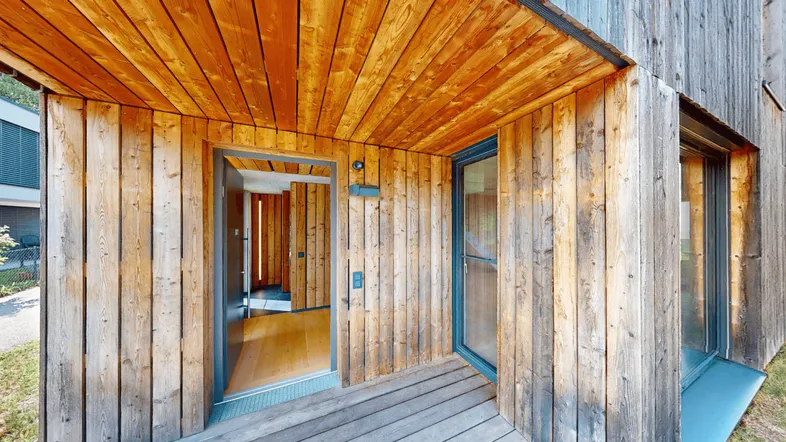 Eingangsbereich des modernen Hauses mit Holzfassade und einer einladenden Holzterrasse.