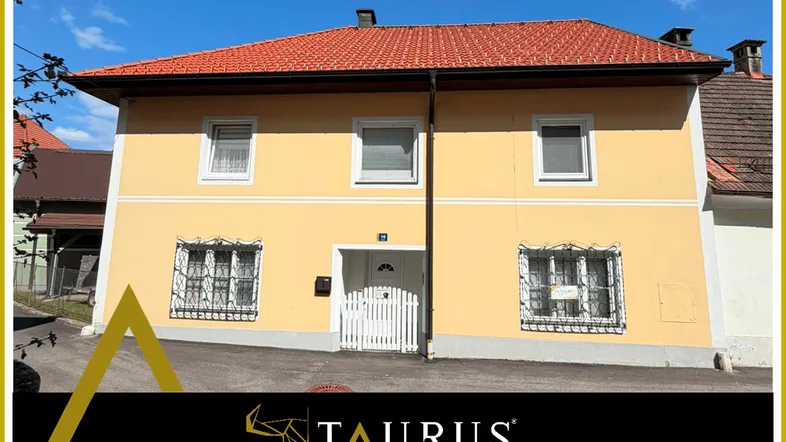 Gelbes Wohnhaus mit rotem Ziegeldach und weißen Fenstern, umgeben von einem kleinen Vorgarten.