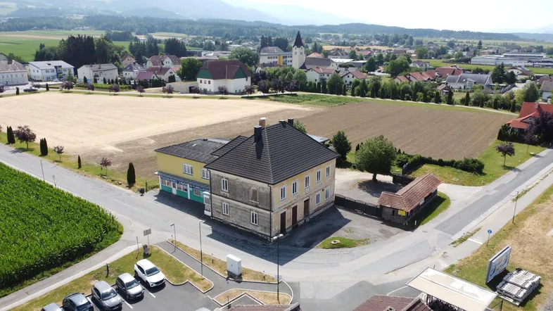 Luftaufnahme eines Gebäudes mit umliegenden Feldern und einem Dorf im Hintergrund.