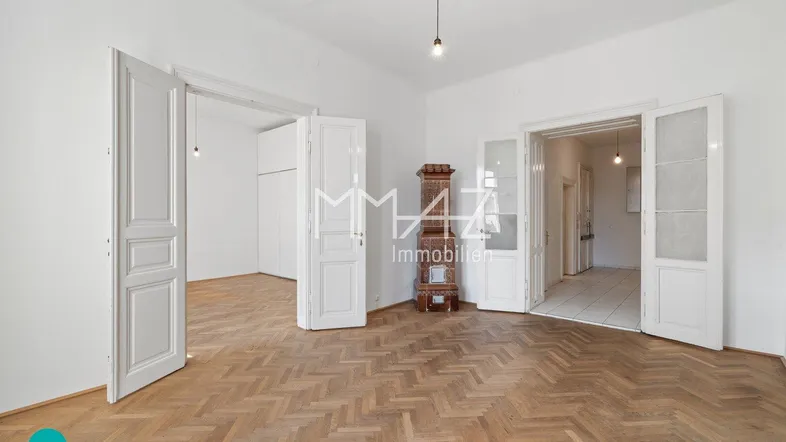 Geräumiges Zimmer mit Fischgrätparkett, hohen Türen und einem traditionellen Kachelofen.
